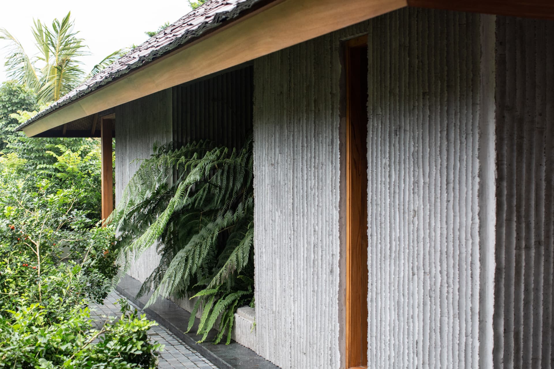 Bamboo-formed concrete facade with ferns and a tiled roof