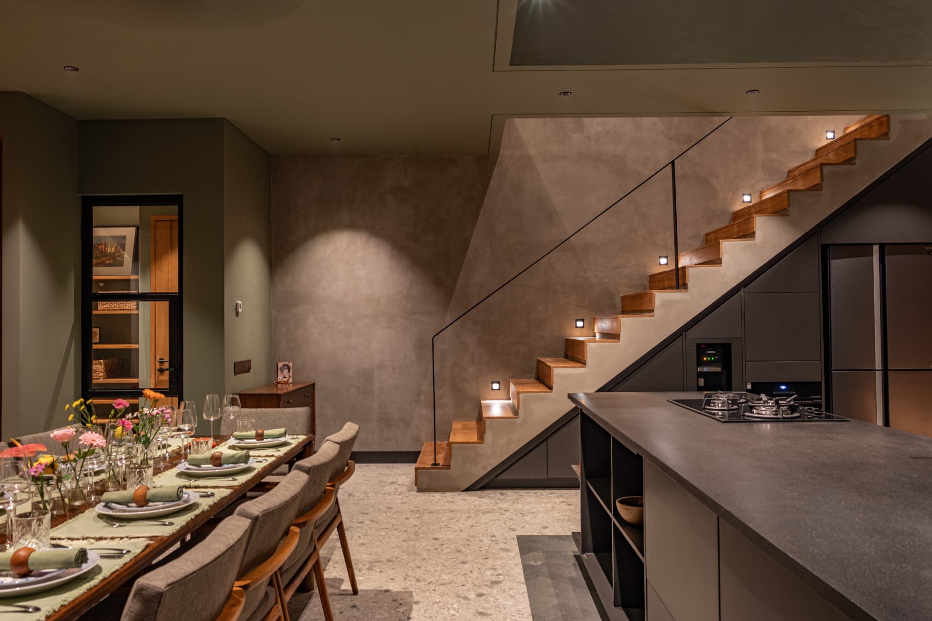 Dining and kitchen with a lit timber stair at night